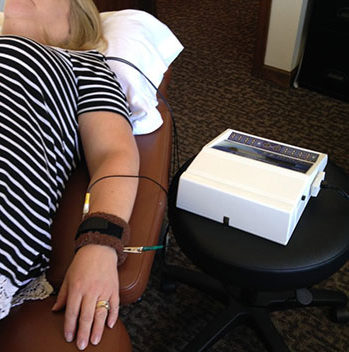 patient laying down while using Frequency Specific Microcurrent machine on wrist