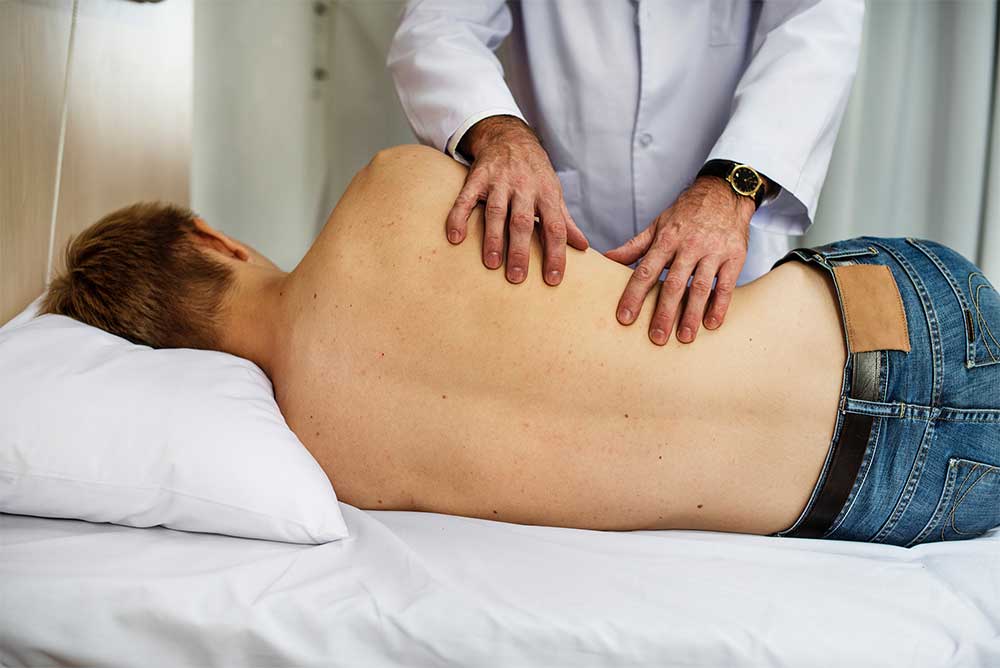 man laying on side with physical therapist touching his back